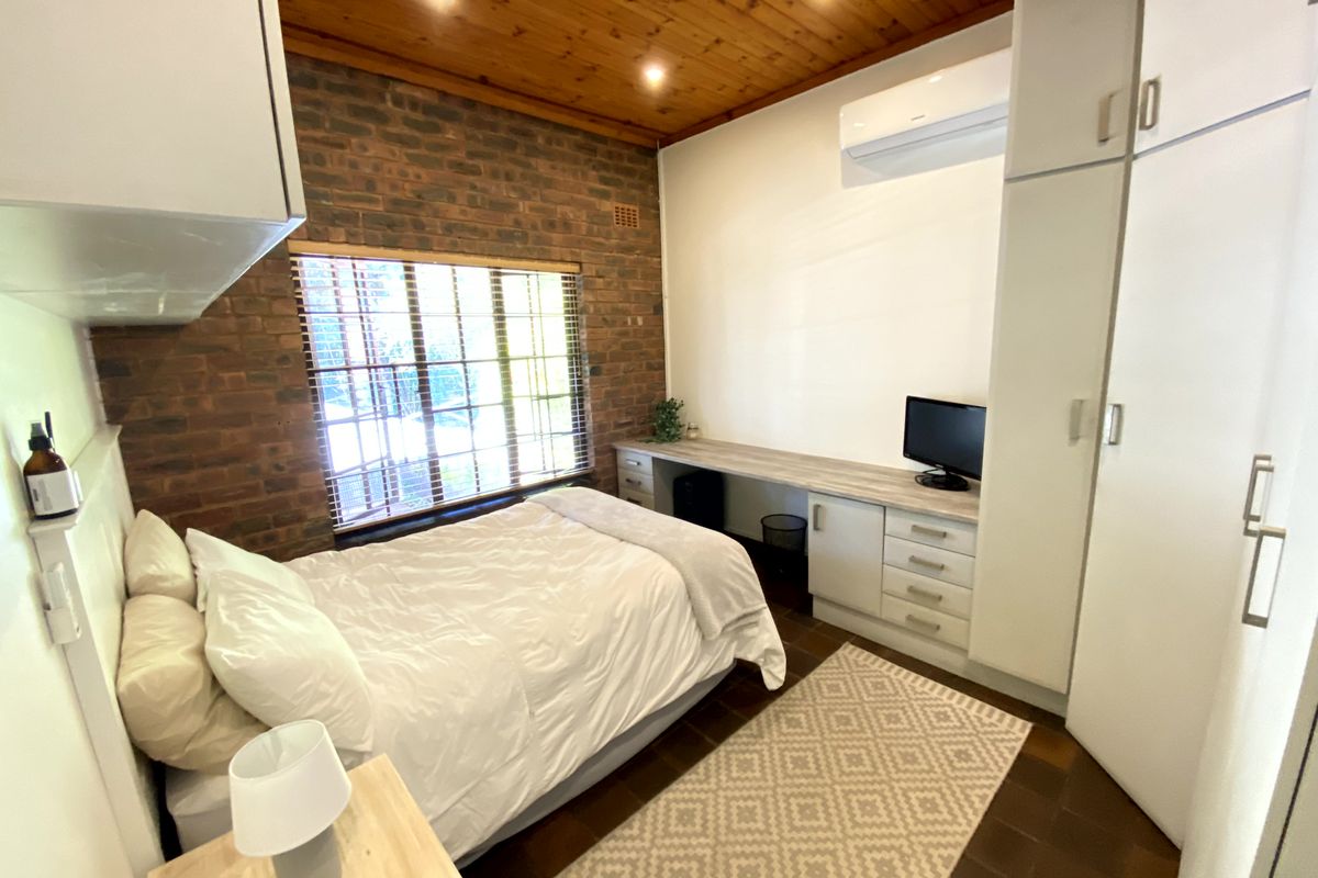 A well-maintained bedroom featuring an exposed brick feature wall, timber ceiling, built-in cabinetry with a desk, and a split-system air conditioner.