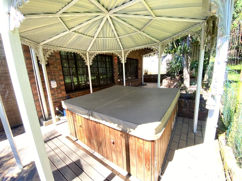 A covered outdoor patio area featuring a gazebo structure, brick walling, and a built-in spa with a protective cover.