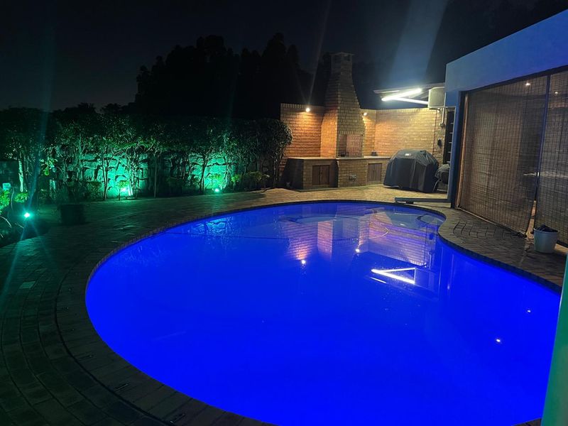 Night view of a swimming pool area featuring a paved patio and a brick built-in braai, perfect for outdoor entertaining.
