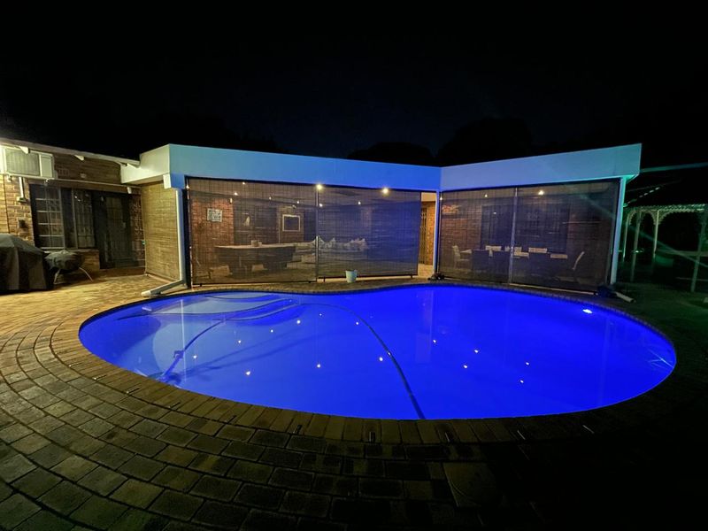 Night view of a swimming pool area featuring brick paving and a covered patio space with integrated lighting.