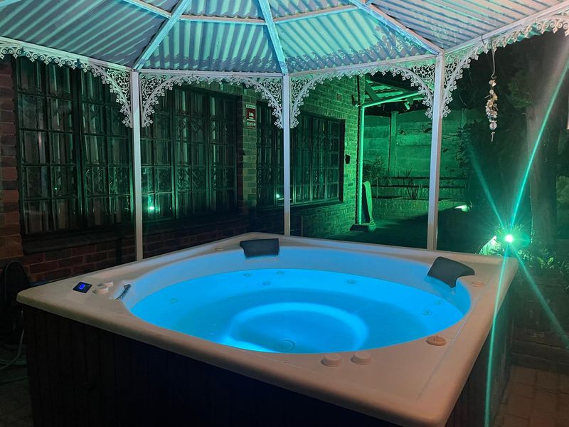 Outdoor entertainment area featuring a built-in hot tub sheltered by a decorative metal gazebo, set against a brick facade at night.