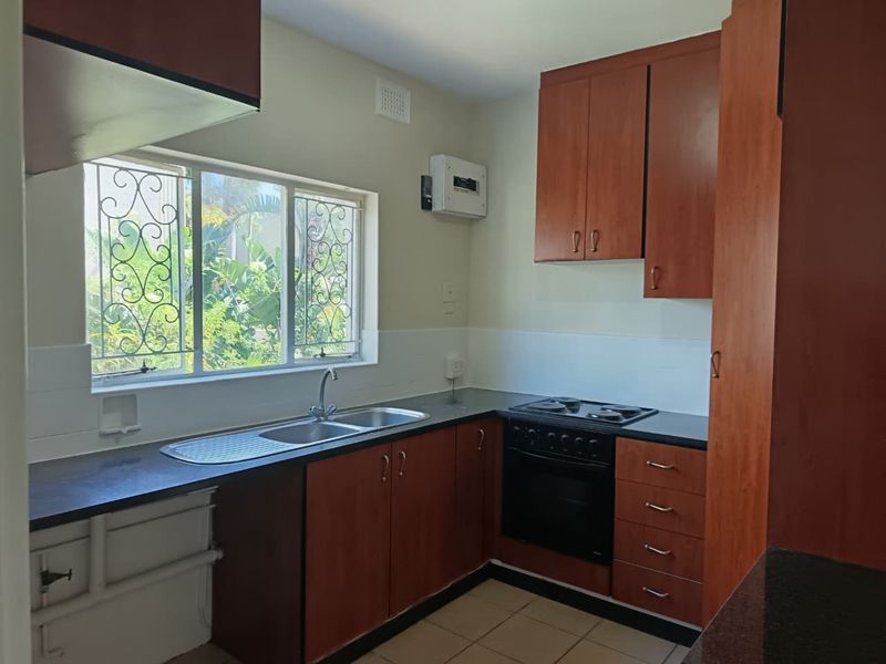 A functional kitchen featuring wood-look cabinetry, laminate countertops, a built-in oven and hob, and a stainless steel sink with security bars on the window.