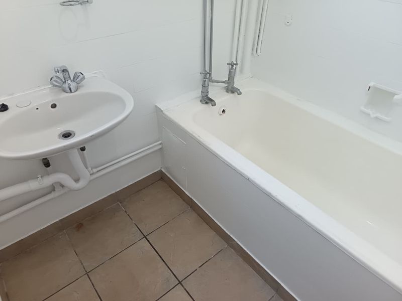 A functional bathroom featuring a standard bathtub, pedestal washbasin, and tiled flooring, currently in need of cosmetic updates and modernization.