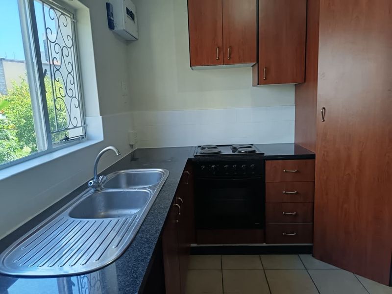 A functional kitchen featuring laminate cabinetry, a double bowl stainless steel sink, built-in oven with electric hob, and tiled flooring.