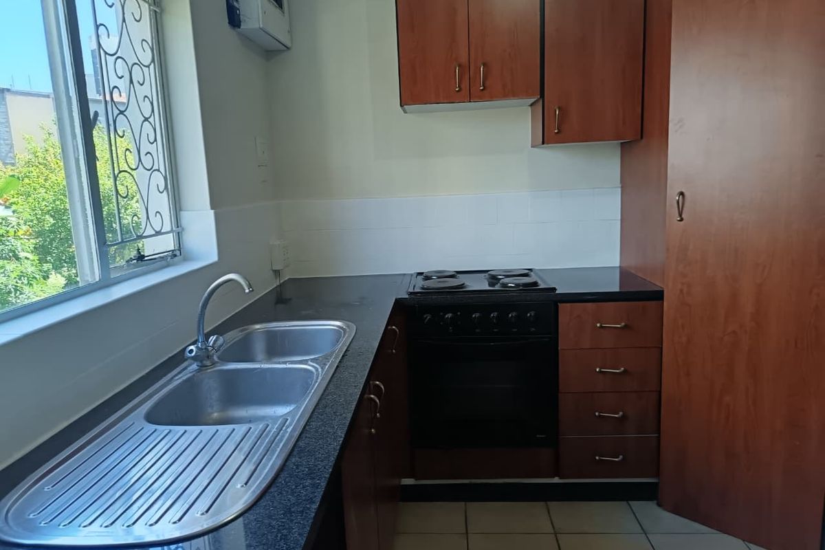 A functional kitchen featuring laminate cabinetry, a double bowl stainless steel sink, built-in oven with electric hob, and tiled flooring.