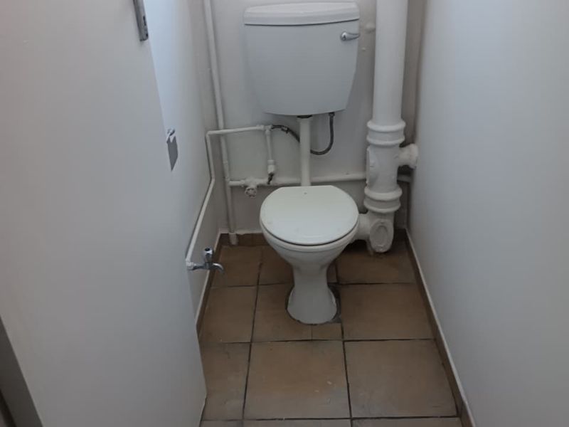 A compact, functional bathroom featuring a standard toilet, tiled flooring, and exposed plumbing fixtures.