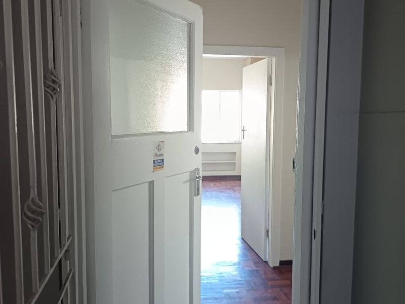 A view through a doorway into a hallway featuring classic parquet flooring and a security gate at the entrance.