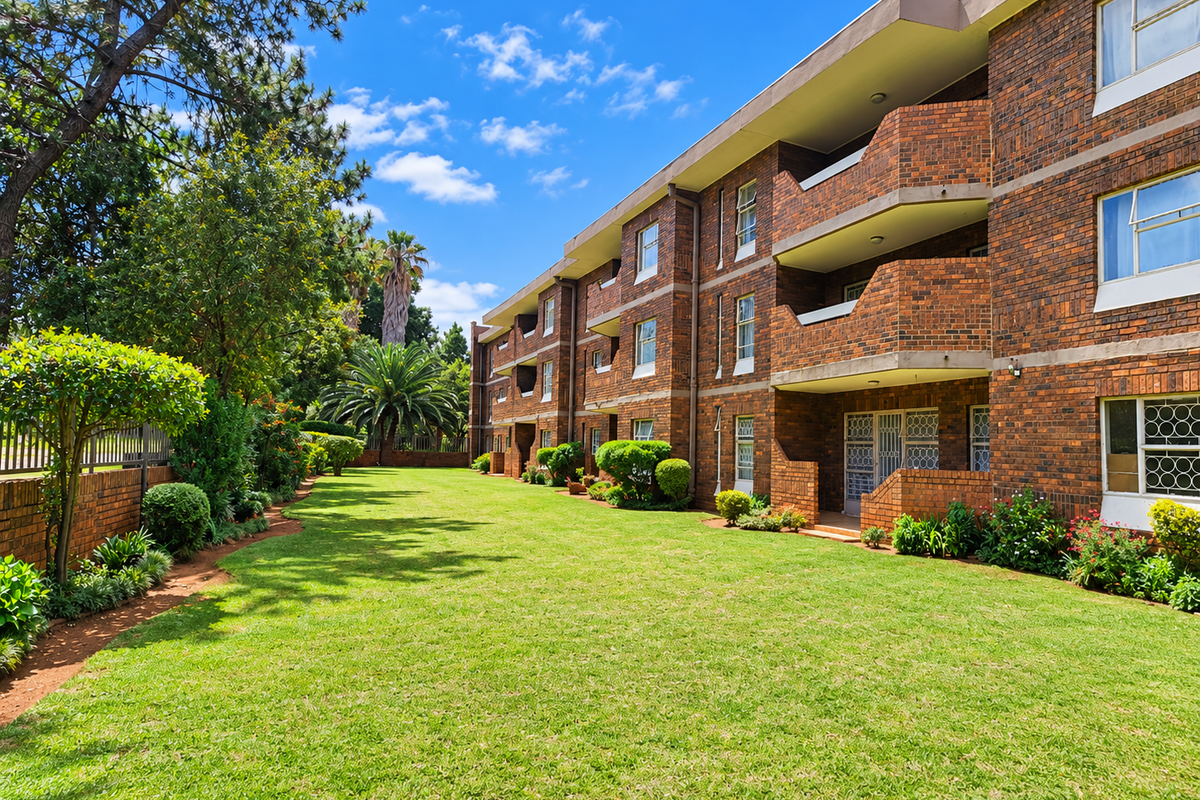 A well-maintained apartment building featuring a face brick facade, private balconies, and a spacious, manicured communal garden area.