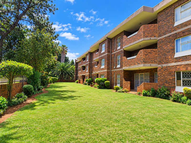 A well-maintained apartment building featuring a face brick facade, private balconies, and a spacious, manicured communal garden area.