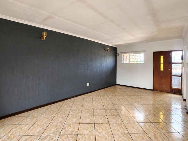 An empty living room featuring tiled flooring, a dark textured feature wall, and a timber entrance door with security gate.