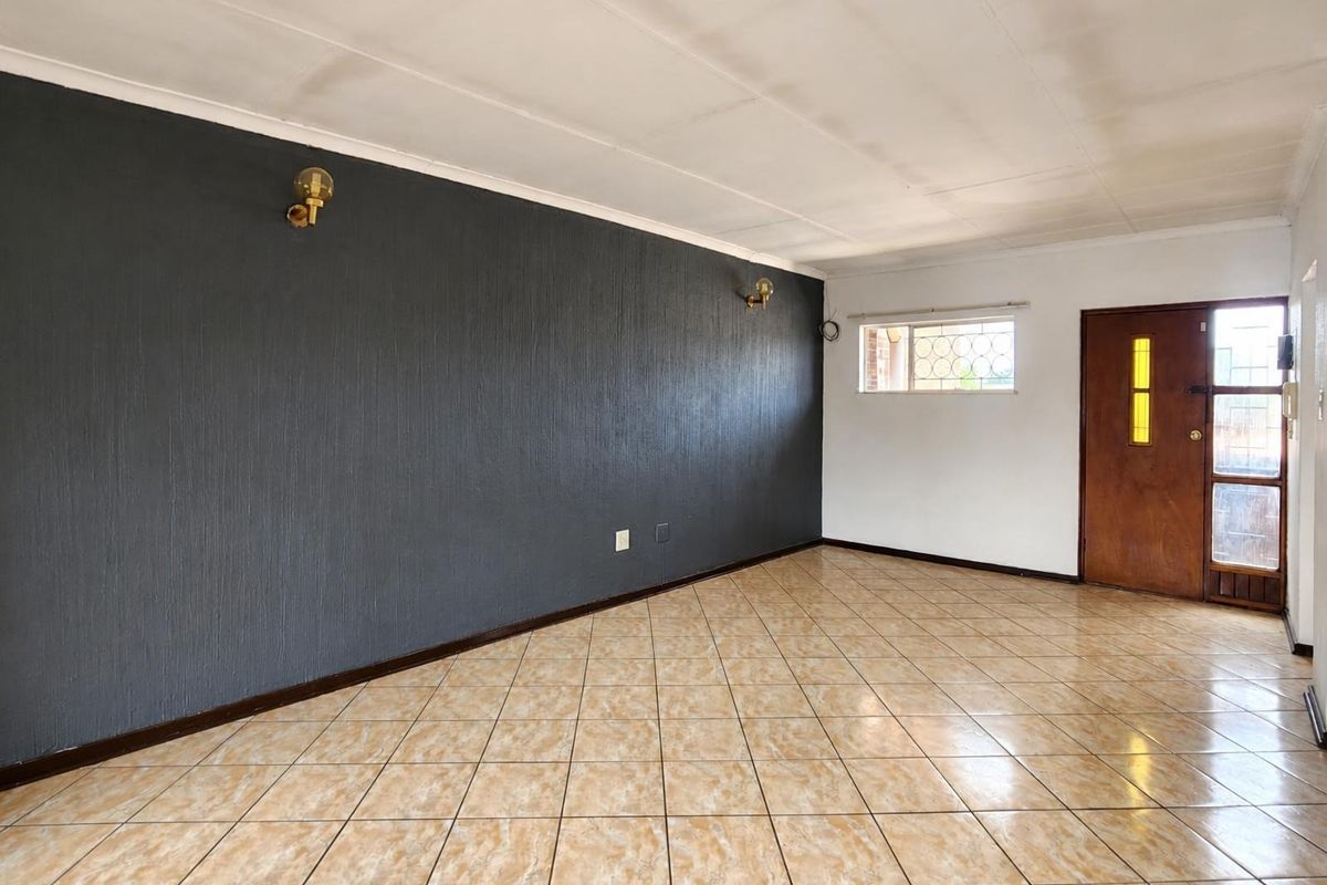 An empty living room featuring tiled flooring, a dark textured feature wall, and a timber entrance door with security gate.