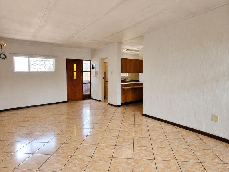 Spacious open-plan living area featuring ceramic tiled flooring, a wooden entrance door, and an adjacent kitchen with built-in cabinetry and a breakfast counter.