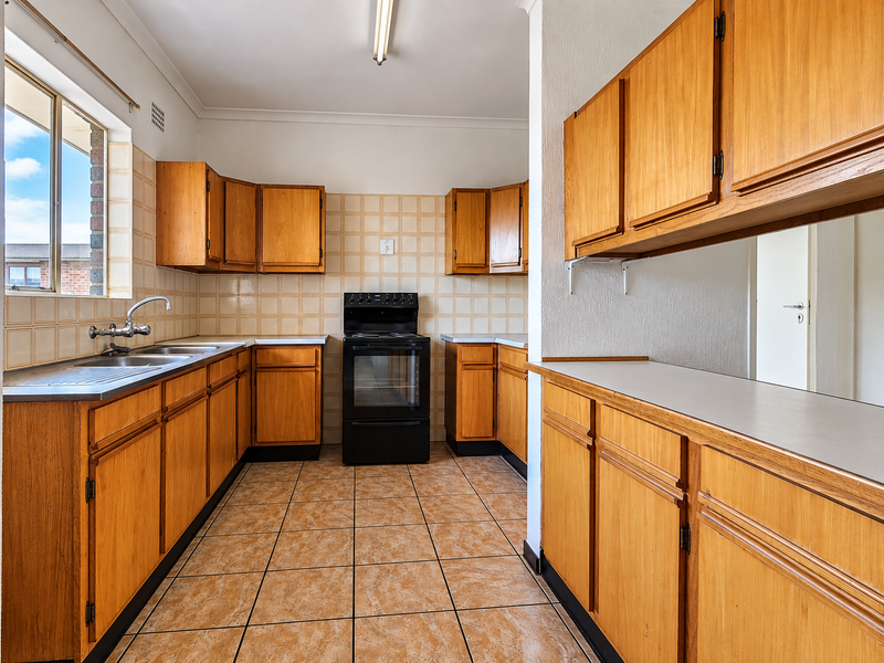 A functional, empty kitchen featuring wooden cabinetry, laminate countertops, a freestanding oven, and tiled finishes, offering a blank canvas for modern renovation.