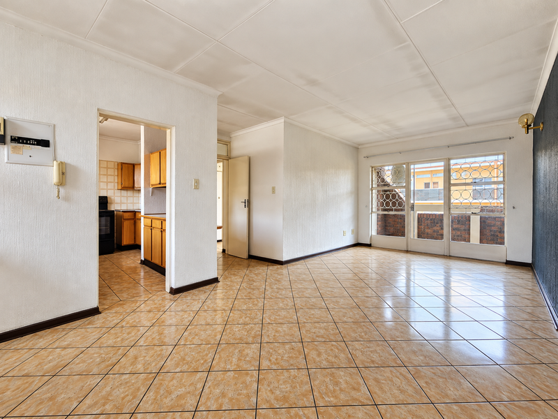Spacious open-plan living area featuring ceramic tiled flooring, direct access to a balcony, and an adjoining kitchen with built-in cabinetry.
