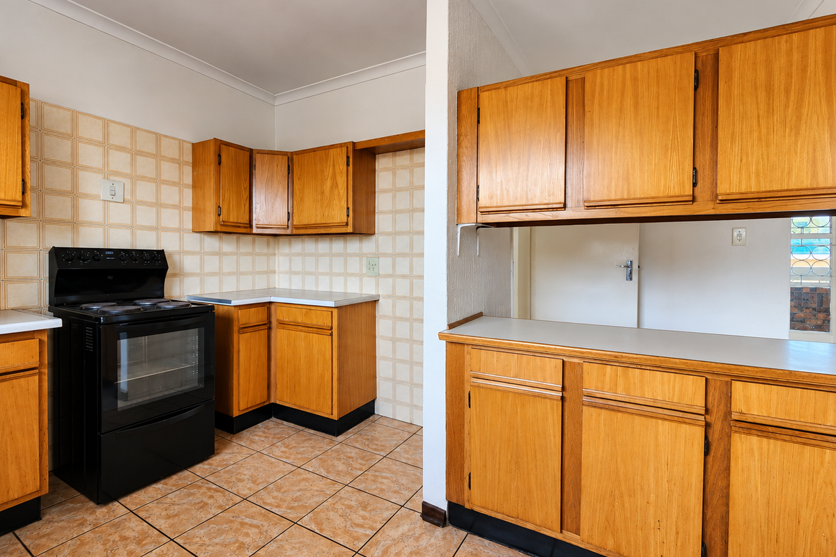 A functional kitchen featuring wooden cabinetry, laminate countertops, and a freestanding electric stove, finished with ceramic wall and floor tiles.