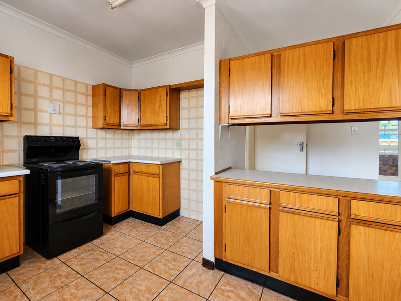A functional kitchen featuring wooden cabinetry, laminate countertops, and a freestanding electric stove, finished with ceramic wall and floor tiles.