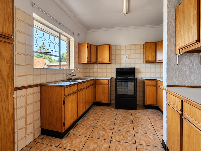 A functional kitchen featuring wooden cabinetry, ceramic tiling, and a freestanding oven, offering a clean space ready for modernization.