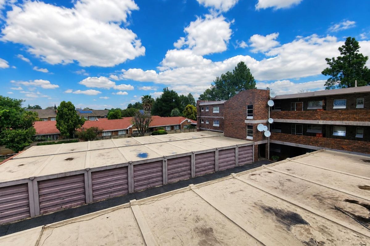 An elevated aerial view showing the exterior of a brick apartment complex and a row of garage units with flat roofing.