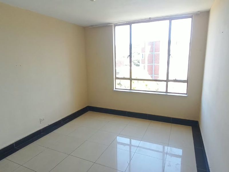A bright, empty bedroom featuring neutral walls, tiled flooring, and a large window providing natural light.