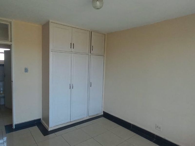 A vacant bedroom featuring built-in cupboards, tiled flooring, and direct access to an adjacent bathroom area.