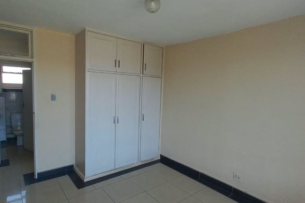 A vacant bedroom featuring built-in cupboards, tiled flooring, and direct access to an adjacent bathroom area.