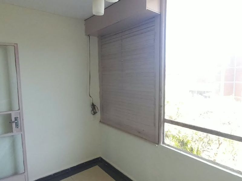 An enclosed balcony or sunroom featuring large windows, a roller shutter, and tiled flooring, offering a bright space with potential for renovation.