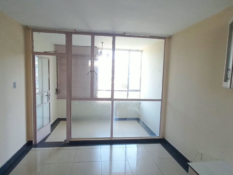 An empty living room featuring tiled flooring, a glass partition wall leading to an enclosed balcony, and wall-mounted storage cabinetry.