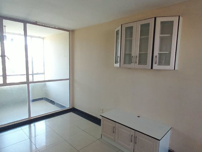 An empty living room featuring tiled floors, built-in storage cabinetry, and an adjoining enclosed balcony with large aluminium-framed windows.