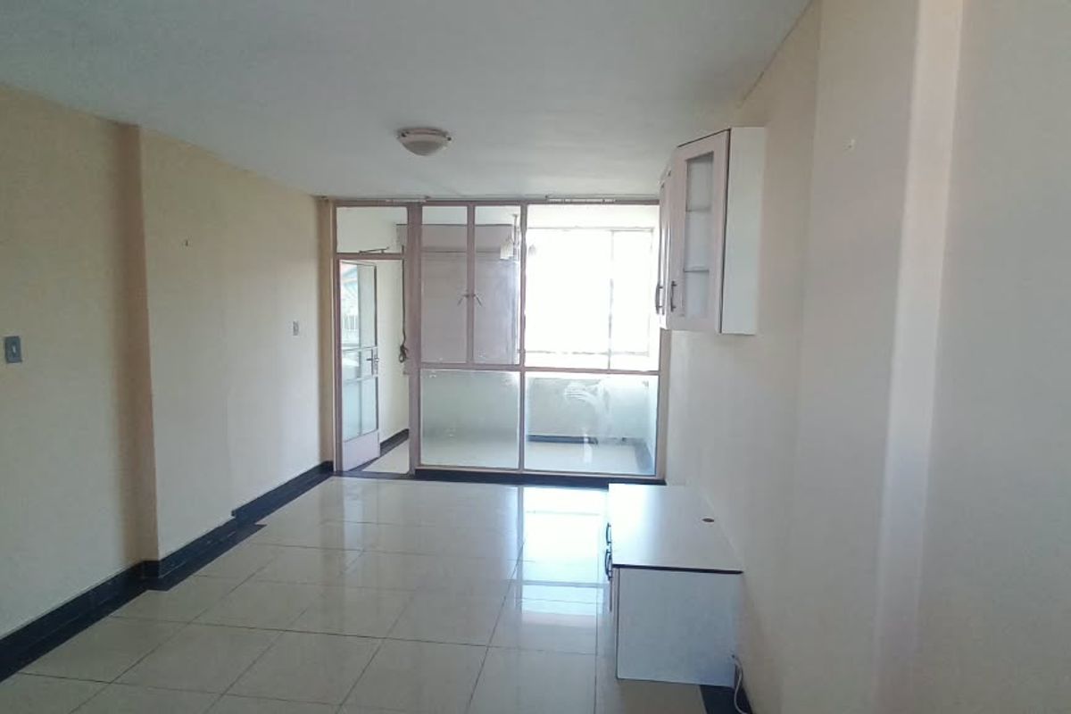 An empty, open-plan living area featuring tiled flooring, neutral walls, and a glass partition leading to an adjacent space.