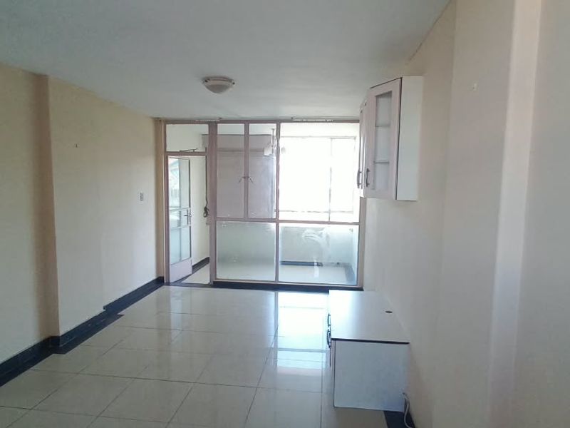 An empty, open-plan living area featuring tiled flooring, neutral walls, and a glass partition leading to an adjacent space.