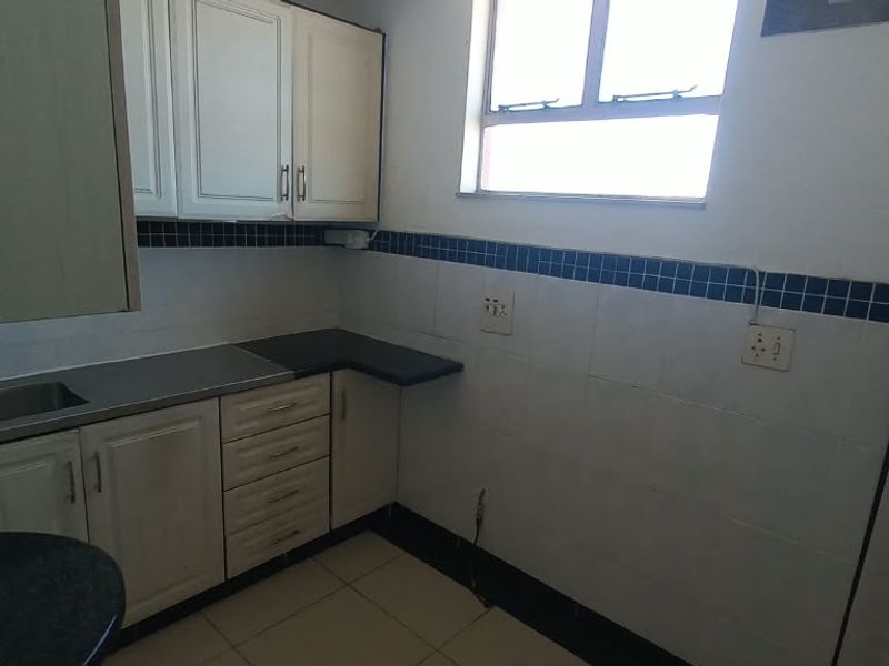 A compact kitchen featuring built-in cabinetry, a stainless steel sink, and tiled backsplash, offering a functional space ready for modernization.