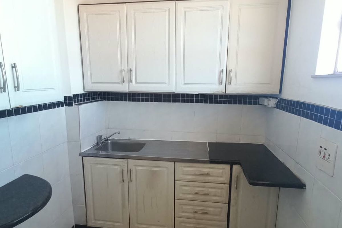 A compact kitchen featuring white built-in cabinetry, a stainless steel sink, and a tiled backsplash with a decorative border.
