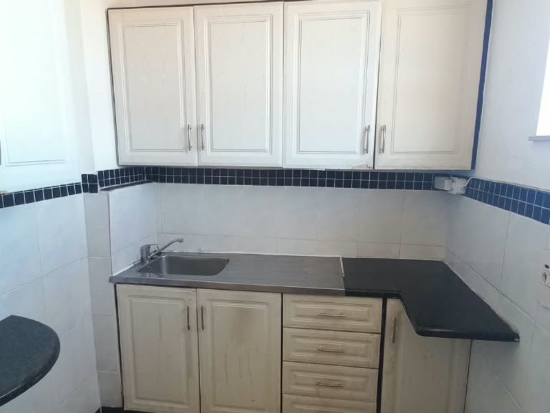 A compact kitchen featuring white built-in cabinetry, a stainless steel sink, and a tiled backsplash with a decorative border.
