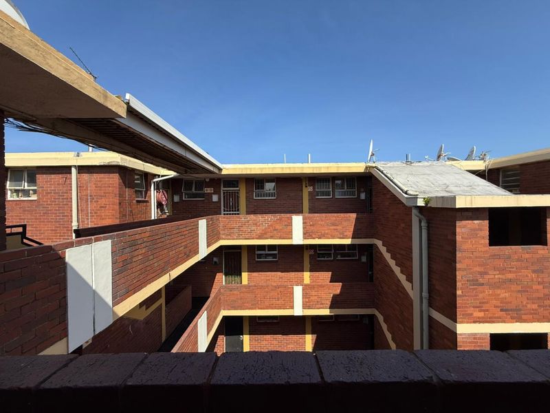 Exterior view of a multi-story brick apartment complex featuring open-air balcony walkways and functional metal security gates.