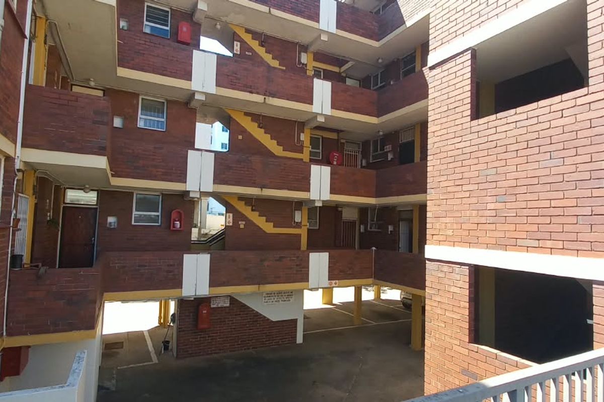 Exterior view of a multi-story apartment complex featuring exposed brickwork, external staircases, and covered walkways providing access to individual units.