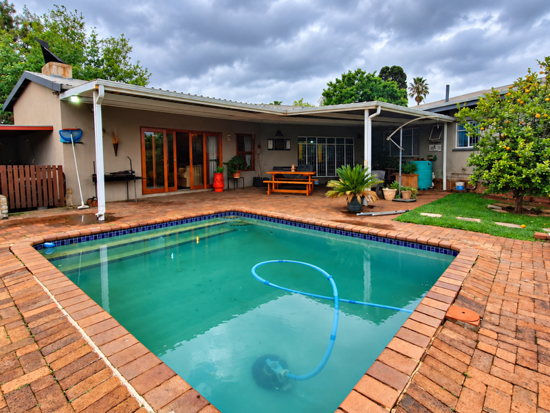 Outdoor pool area featuring a swimming pool, covered patio space, and brick paved surround, providing a functional area for outdoor relaxation.