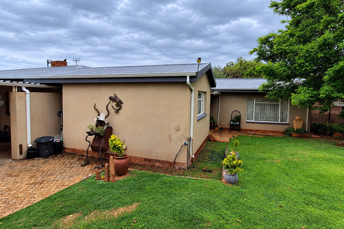Rear view of the house featuring a lawn, paved patio area, and corrugated metal roofing.