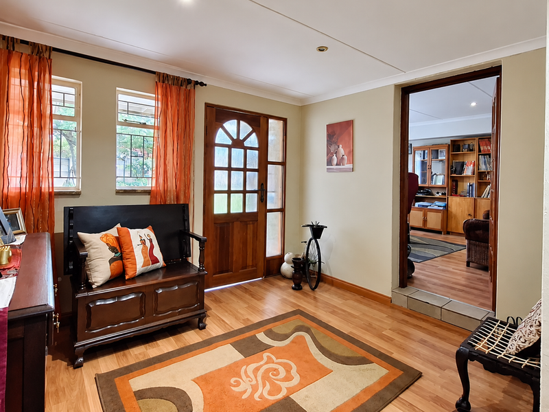 A welcoming entrance hall featuring timber flooring, a solid wood front door with glass panels, and recessed lighting, leading into an adjacent living space.