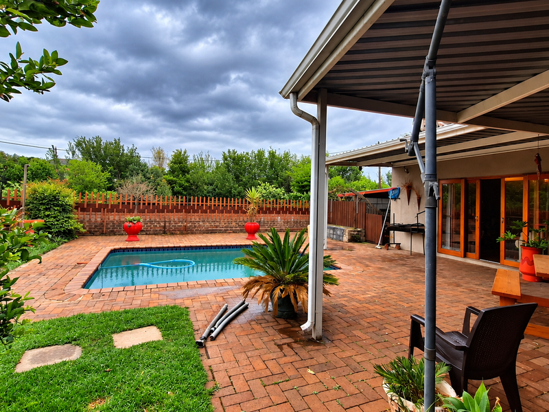 Outdoor pool area featuring a brick-paved patio, covered entertainment space, and a swimming pool enclosed by a brick and timber boundary wall.