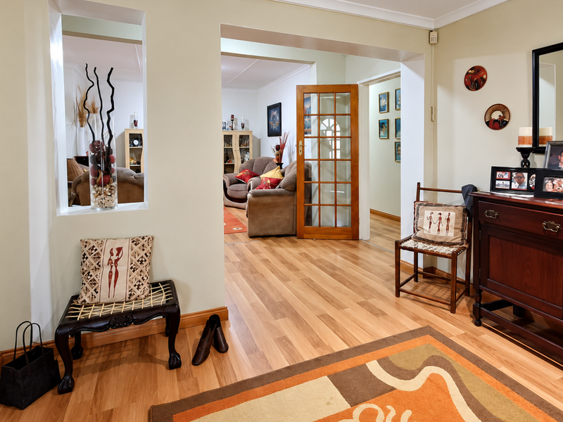 A bright hallway featuring laminate flooring, a timber-framed glass door, and a pass-through window connecting to the adjacent living space.