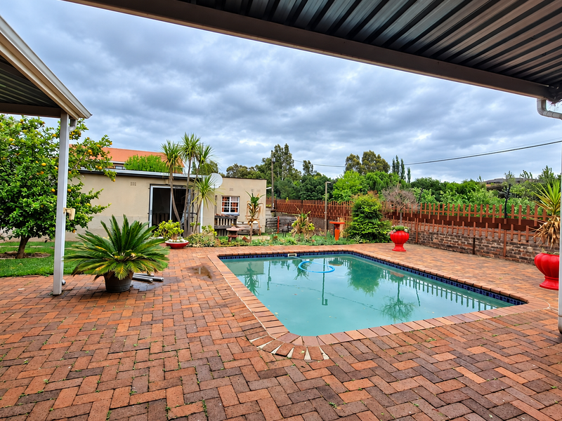 Outdoor pool area featuring a swimming pool, brick paved surround, and a covered patio area under a metal roof structure.