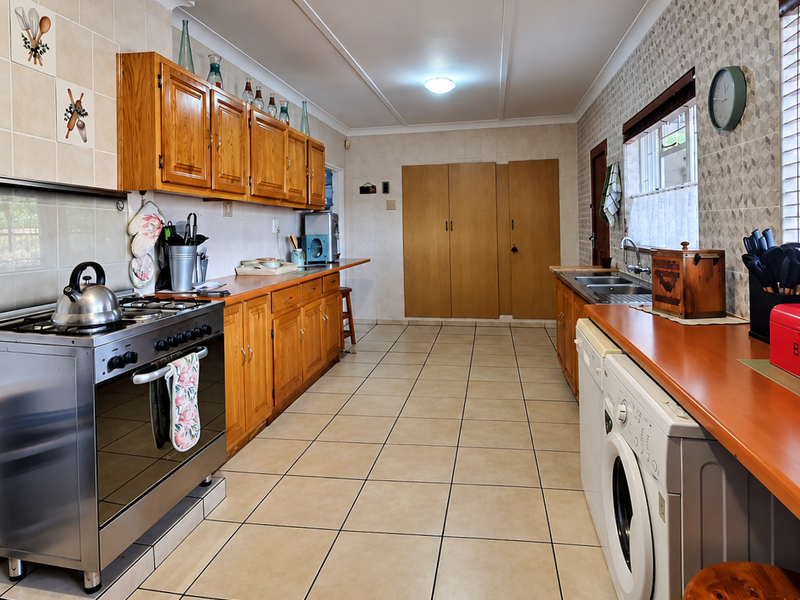 Spacious kitchen featuring wooden cabinetry, tiled flooring, a stainless steel gas stove, and ample counter space with integrated laundry facilities.