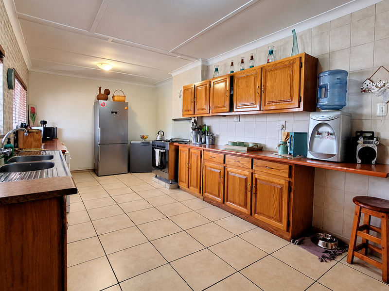 A functional kitchen featuring wooden cabinetry, tiled backsplash, and tiled flooring, equipped with a built-in oven and hob.