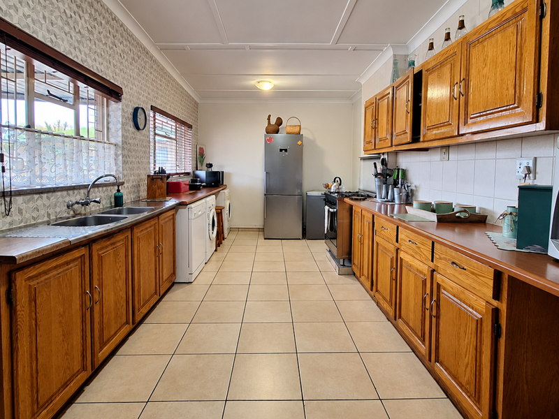 A functional galley-style kitchen featuring wooden cabinetry, laminate countertops, tiled flooring, and a tiled backsplash with integrated appliance spaces.