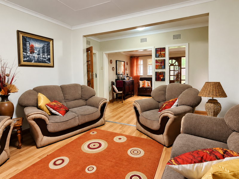 A comfortable living room featuring hardwood flooring and coved ceilings, with an open transition leading into an adjacent secondary living or dining space.
