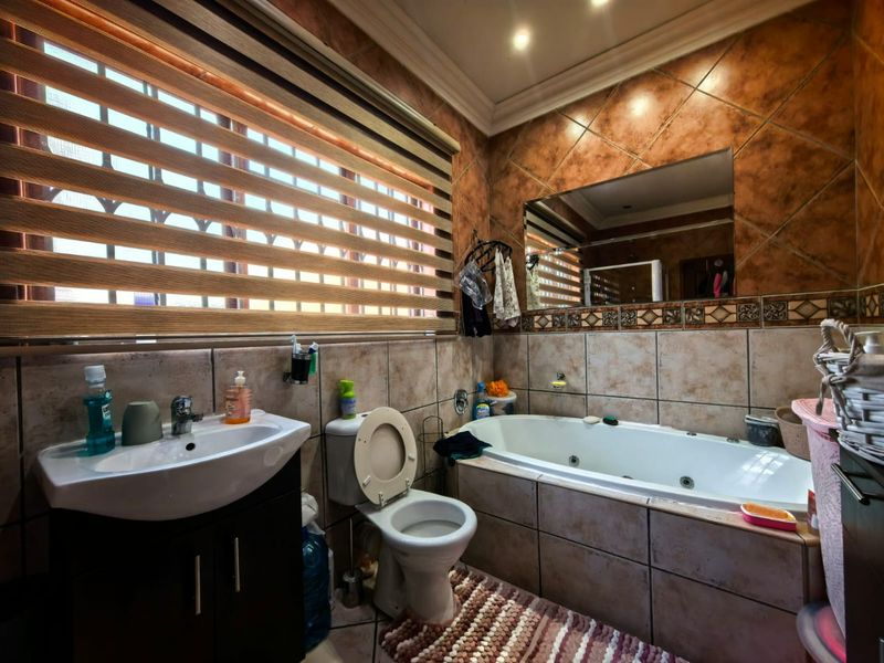 A functional bathroom featuring a built-in bathtub, vanity basin, toilet, and tiled wall finishes, illuminated by recessed downlights.