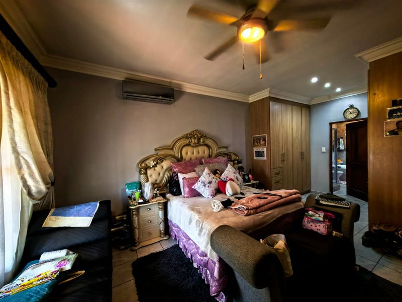 A spacious bedroom featuring built-in cupboards, an air conditioning unit, a ceiling fan, and tiled flooring, with an adjoining en-suite bathroom.