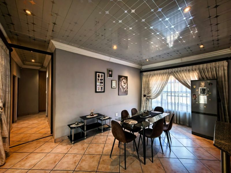 A dining area featuring tiled flooring, decorative ceiling panels with recessed lighting, and coved cornicing, providing a functional space for family meals.