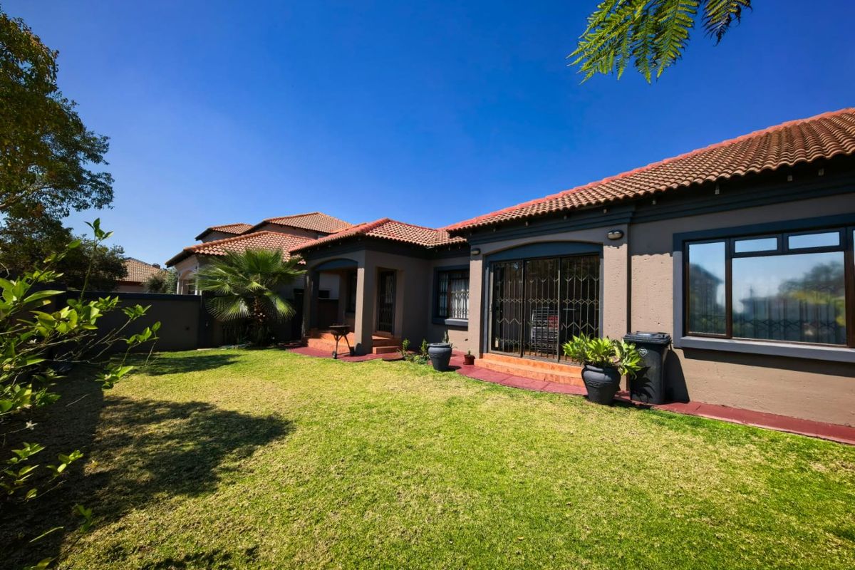 A well-maintained rear exterior view of the house featuring a landscaped lawn, paved patio area, and terracotta tiled roof.
