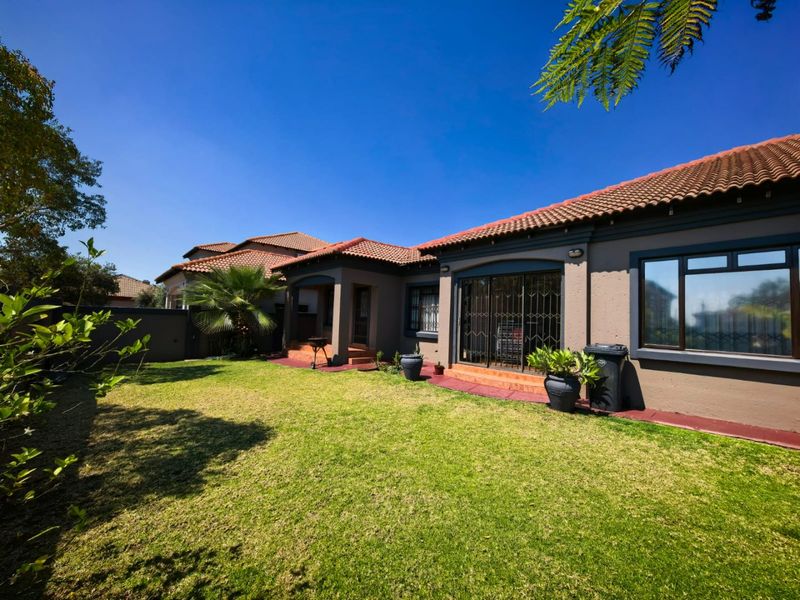 A well-maintained rear exterior view of the house featuring a landscaped lawn, paved patio area, and terracotta tiled roof.